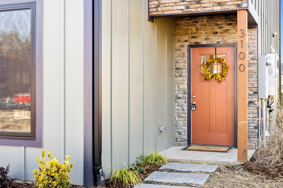 Modern house entrance with an autumn wreath on a red door, surrounded by stone and wood accents.
